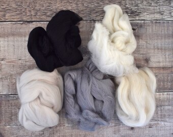 May include: Five balls of wool in different colors: black, white, gray, cream, and off-white. The balls are arranged on a wooden surface.