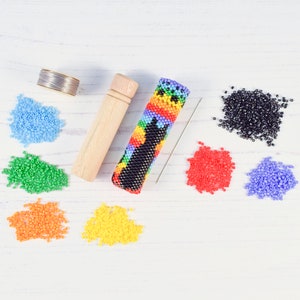 May include: A colorful beaded case for a needle, along with a spool of thread, a wooden needle holder, and a variety of colored beads.