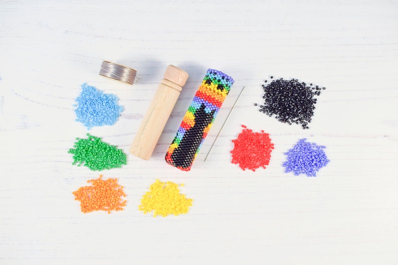 May include: A colorful beaded case for a needle, along with a spool of thread, a wooden needle holder, and a variety of colored beads.