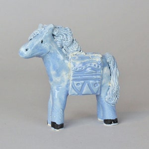 May include: A light blue ceramic horse figurine with a saddle and a detailed mane. The horse has black hooves and a white glaze.