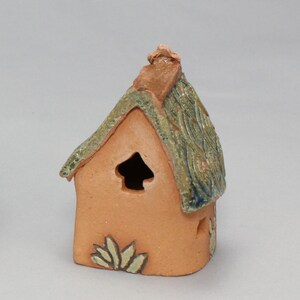 May include: A small, hand-crafted ceramic house with a green and brown roof, a small window, and a decorative design on the front.