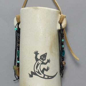 May include: A white ceramic hanging planter with a black lizard design and turquoise and brown beads hanging from the bottom.
