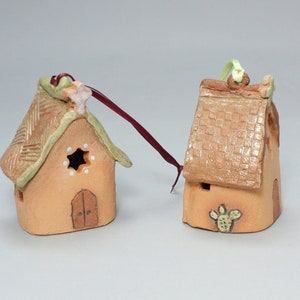 May include: Two small, hand-painted ceramic houses with a rustic, southwestern style. One house has a green roof with a star and the other has a brown roof with a cactus.