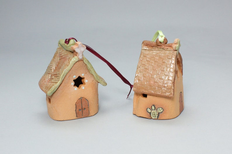 May include: Two small, hand-painted ceramic houses with a rustic, southwestern style. One house has a green roof with a star and the other has a brown roof with a cactus.