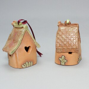 May include: Two small ceramic houses with green and brown glaze. One house has a heart-shaped window and a red ribbon. The other house has a cactus design.