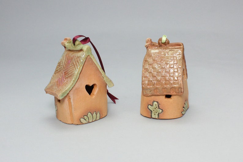 May include: Two small ceramic houses with green and brown glaze. One house has a heart-shaped window and a red ribbon. The other house has a cactus design.