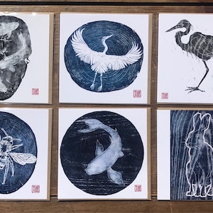 Puede incluir: Conjunto de seis grabados cuadrados con ilustraciones estilo xilografía. Las imágenes muestran carpas koi, una grulla, una garza, una abeja, un pez koi y un conejo en azul y blanco, con un sello rojo en la esquina.