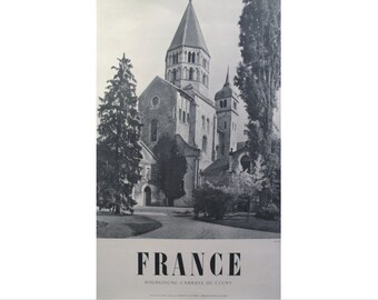 May include: A black and white photograph of the Abbey of Cluny in Burgundy, France. The photo shows the abbey's tall, pointed tower and surrounding buildings.