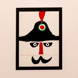 May include: A vintage Italian film poster with a stylized face design. It features a black hat, mustache, and eyes, with a red nose and a red, white, and green circular emblem. Text is visible at the bottom of the poster.