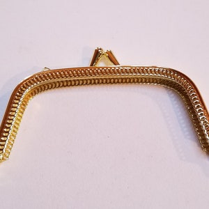 May include: Gold-toned metal purse frame with a decorative, textured edge. The frame is open and ready to be attached to a purse.