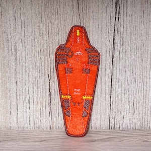 Könnte beinhalten: Ein orangefarbener Filzaufnäher mit rotem Rand. Der Aufnäher hat eine Schildform mit braunen und gelben Stickdetails. Der Text "Z-UX" und "DMW" ist auf dem Aufnäher zu sehen.