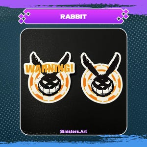 Könnte beinhalten: Zwei Aufkleber mit einem schwarzen Kaninchenkopf mit einem bedrohlichen Grinsen, vor einem weißen und orangefarbenen kreisförmigen Design. Ein Aufkleber hat das Wort "WARNING!" in Orange. Das Wort "Rabbit" steht oben.