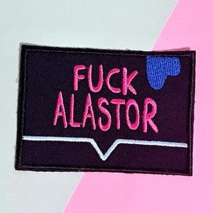 May include: Embroidered patch with the text "FUCK ALASTOR" in pink, above a white line and a blue shape on a black background. The patch is rectangular with a black border. The background is a mix of pink and white.