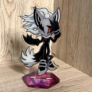 May include: A clear acrylic standee featuring a stylised anthropomorphic character with white spiky hair, a grey mask with black markings, and a single red eye. The character wears a black suit and stands on a hexagonal purple base with geometric patterns.