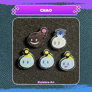 May include: Five acrylic charms featuring Chao characters. The charms include a dark brown Chao with a pink pom-pom, a white Chao with a blue halo, and three blue Chao with yellow accents. The word "CHAO" is displayed at the top.