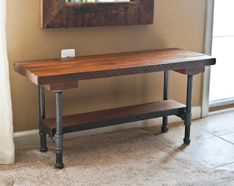 May include: A rustic wooden bench with a black metal frame and a single shelf. The bench is made from reclaimed wood and has a natural finish. The metal frame is made from industrial pipes and has a black powder coat finish.
