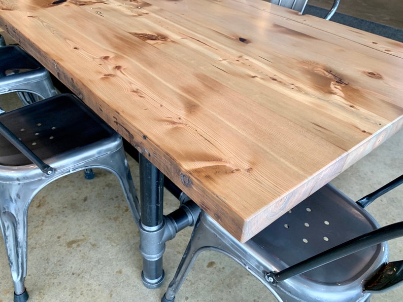 May include: A wooden table top with a natural wood finish and a black metal pipe base. The table is paired with two metal chairs with black metal frames.