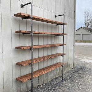 May include: A rustic industrial shelf unit with six wooden shelves supported by black metal pipes. The shelves are made of reclaimed wood and have a dark brown stain. The unit is mounted to a white wall.
