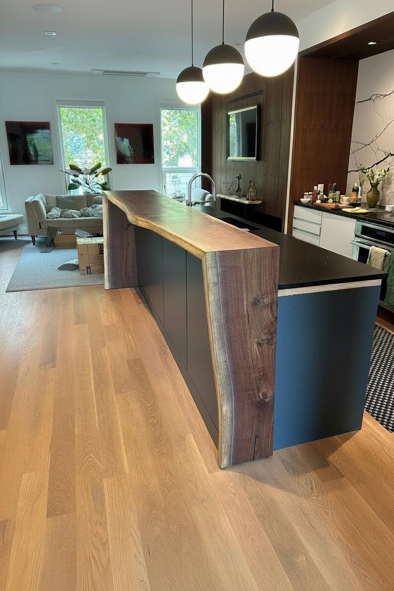 May include: A kitchen island featuring a natural live edge walnut wood countertop that extends down the side panel. The base of the island is finished in a matte dark gray color, contrasting with the warm brown tones of the wood grain.
