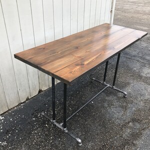 May include: A rectangular wooden table with a dark brown finish. The tabletop is supported by black metal pipes and fittings. The table is approximately 48 inches long and 24 inches wide, ideal for a home or office setting.
