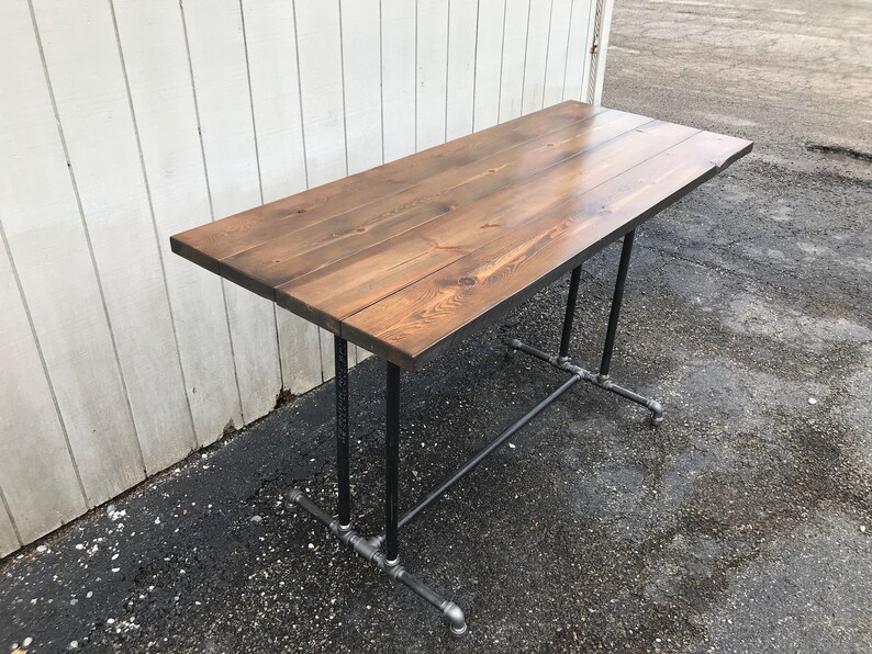 May include: A rectangular wooden table with a dark brown finish. The tabletop is supported by black metal pipes and fittings. The table is approximately 48 inches long and 24 inches wide, ideal for a home or office setting.
