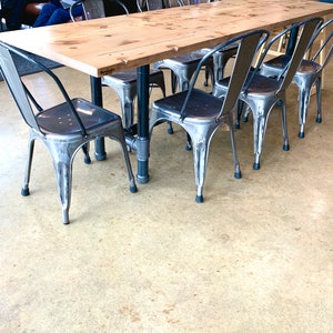 May include: A wooden table with a light wood finish and six metal chairs with black legs. The chairs are arranged around the table, and the floor is a light beige color.