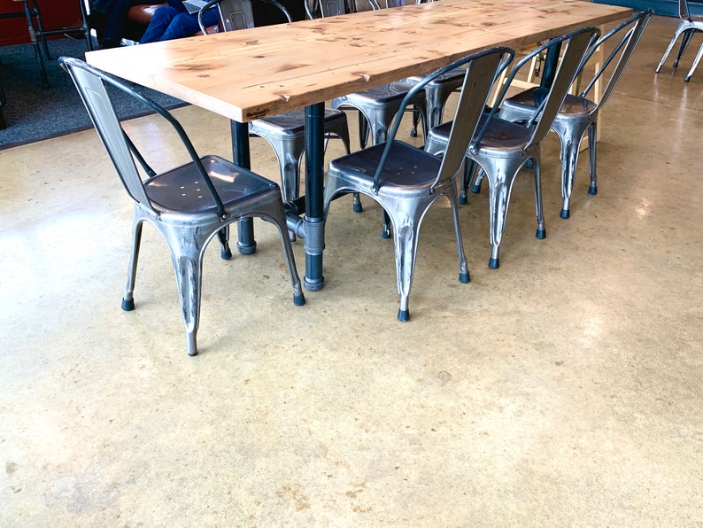 May include: A wooden table with a light wood finish and six metal chairs with black legs. The chairs are arranged around the table, and the floor is a light beige color.