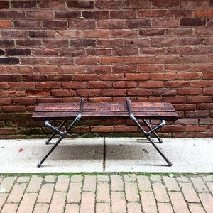 May include: A rustic wooden bench with black metal legs. The bench is made of reclaimed wood and has a natural finish. The legs are made of industrial pipe and have a black powder coat finish.