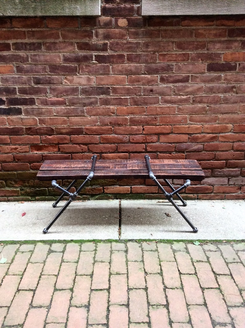 May include: A rustic wooden bench with black metal legs. The bench is made of reclaimed wood and has a natural finish. The legs are made of industrial pipe and have a black powder coat finish.
