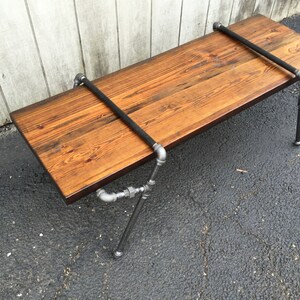 May include: A rustic wooden coffee table with a dark wood stain. The table has a metal frame made of black pipes and fittings. The table top has a heart carved into it with the date "1970" inscribed.