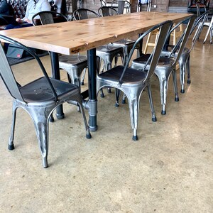 May include: A wooden table with a metal frame and six metal chairs. The chairs have a silver finish and black rubber feet. The table has a light wood finish and a black metal frame.