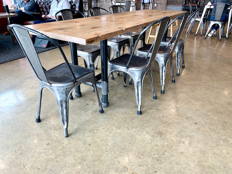 May include: A wooden table with a metal frame and six metal chairs. The chairs have a silver finish and black rubber feet. The table has a light wood finish and a black metal frame.