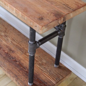 May include: A rustic wooden console table with two shelves, supported by black metal pipe legs. The table has a natural wood finish and a distressed look.