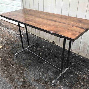 May include: A rectangular wooden table with a dark brown finish. The tabletop is supported by black metal pipes and fittings, creating an industrial design. The table is approximately 152 cm long.