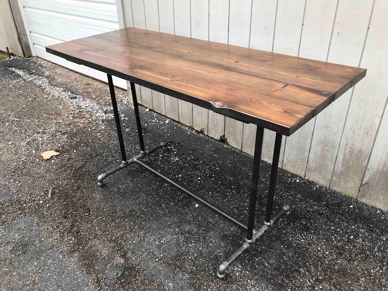 May include: A rectangular wooden table with a dark brown finish. The tabletop is supported by black metal pipes and fittings, creating an industrial design. The table is approximately 152 cm long.