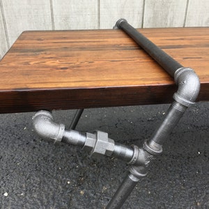May include: A rustic wooden table with a black stained top and a metal pipe frame. The table has a simple design with a single pipe rail across the top.