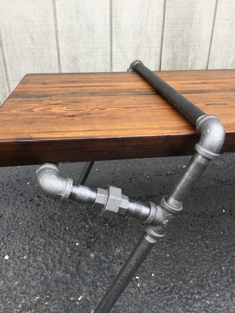 May include: A rustic wooden table with a black stained top and a metal pipe frame. The table has a simple design with a single pipe rail across the top.
