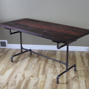 May include: A rectangular desk with a dark stained wooden top and black pipe legs. The tabletop is made of several wooden planks. The desk is approximately 60 inches long and 30 inches wide.