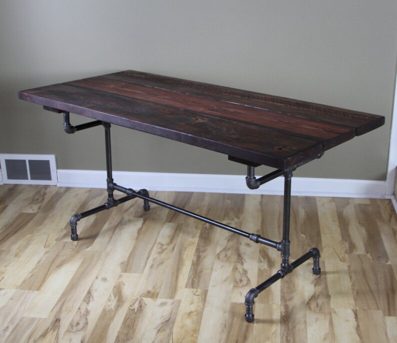 May include: A rectangular desk with a dark stained wooden top and black pipe legs. The tabletop is made of several wooden planks. The desk is approximately 60 inches long and 30 inches wide.