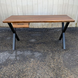 May include: A wooden desk with a single drawer and black metal legs. The desk has a live edge top and a natural wood finish.