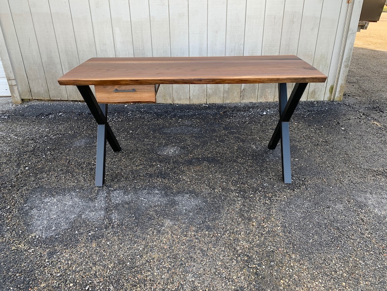 May include: A wooden desk with a single drawer and black metal legs. The desk has a live edge top and a natural wood finish.