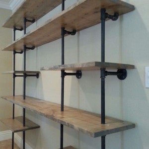 May include: A set of black metal pipe shelves with wooden shelves. The shelves are mounted to a wall and are empty.