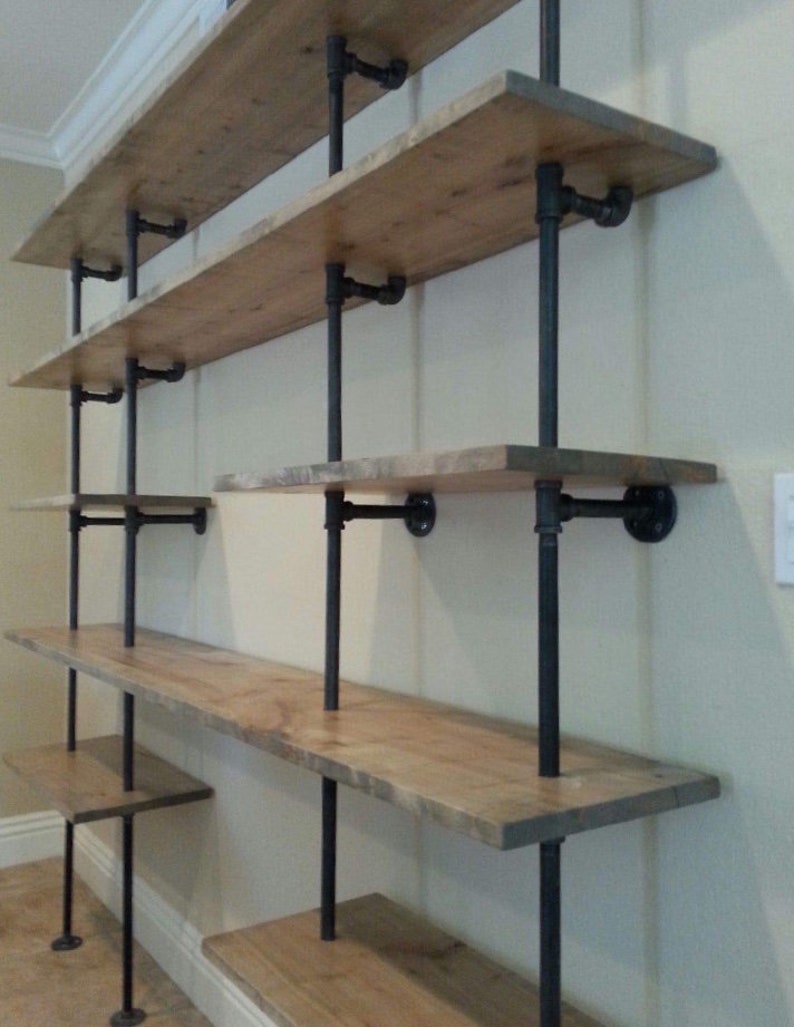 May include: A set of black metal pipe shelves with wooden shelves. The shelves are mounted to a wall and are empty.