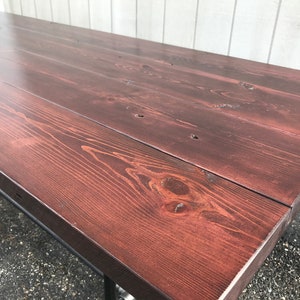 May include: A large, rectangular wooden table with a rich, dark reddish-brown stain. The tabletop is constructed from several planks, showcasing the natural wood grain. The table has metal legs.
