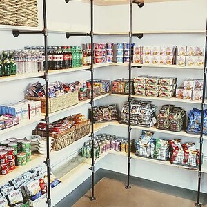 May include: A corner pantry with black metal pipe shelving stocked with canned goods, snacks, and beverages. The shelves are labeled "Southern BBQ".