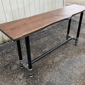 May include: A long, dark brown wooden bar table with a live edge top and black metal pipe legs.