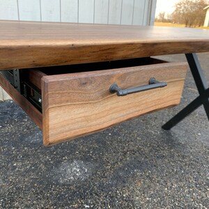 May include: A wooden desk with a black metal X-shaped base and a single drawer with a black metal handle.