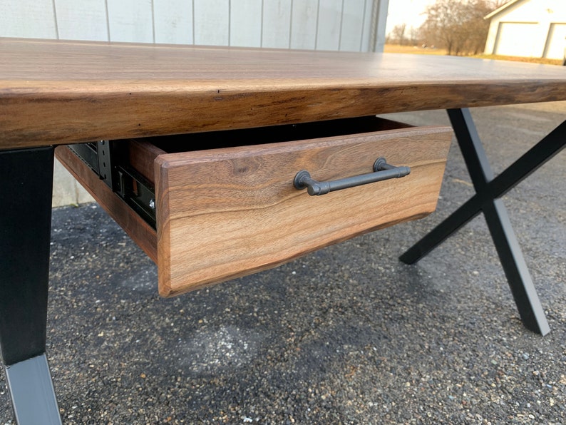 May include: A wooden desk with a black metal X-shaped base and a single drawer with a black metal handle.