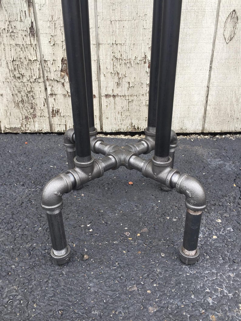 May include: Close-up of the base of a black metal table with four legs. The legs are made of pipe fittings and are connected to a central cross-shaped piece.