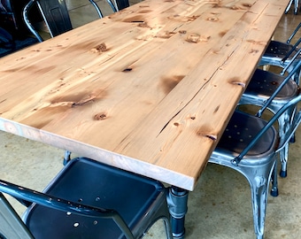 May include: A long, wooden table with a natural finish and a distressed look. The table is surrounded by black metal chairs with a distressed silver finish.
